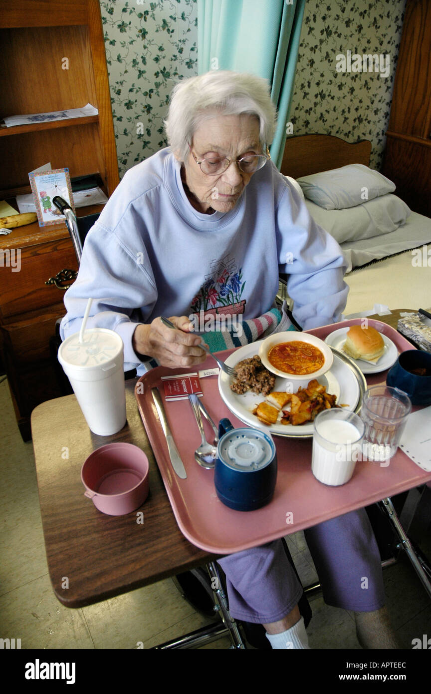 A senior female receives assistance by being served food and meals in a nursing home rehabilitation center Stock Photo