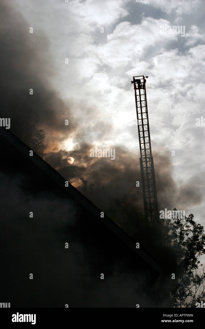 A ladder extended above the smoke coming from a house structure fire getting ready to pump water onto the fire Stock Photo