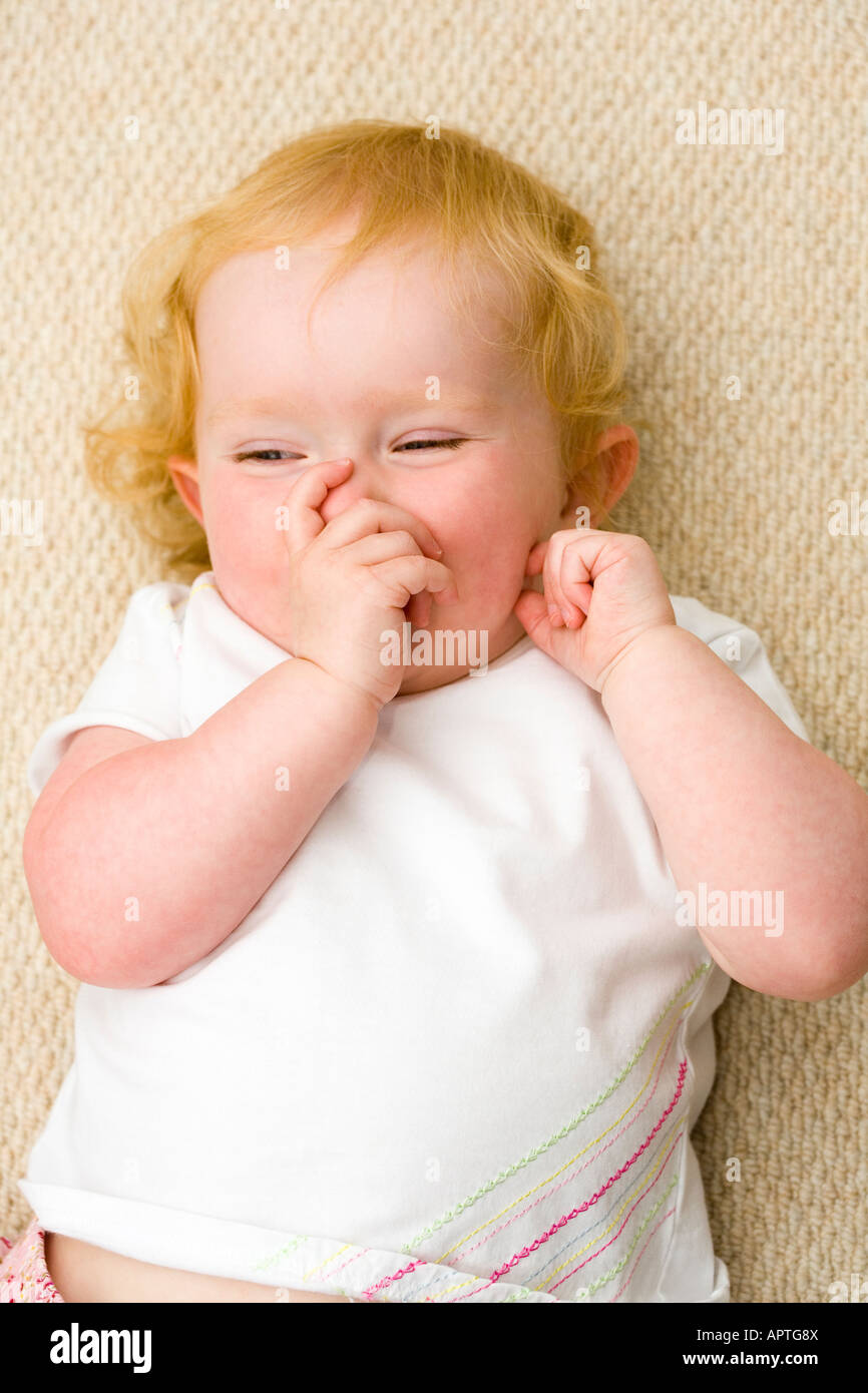 Female Strawberry Blonde Toddler Lying On Beige Carpet Sucking