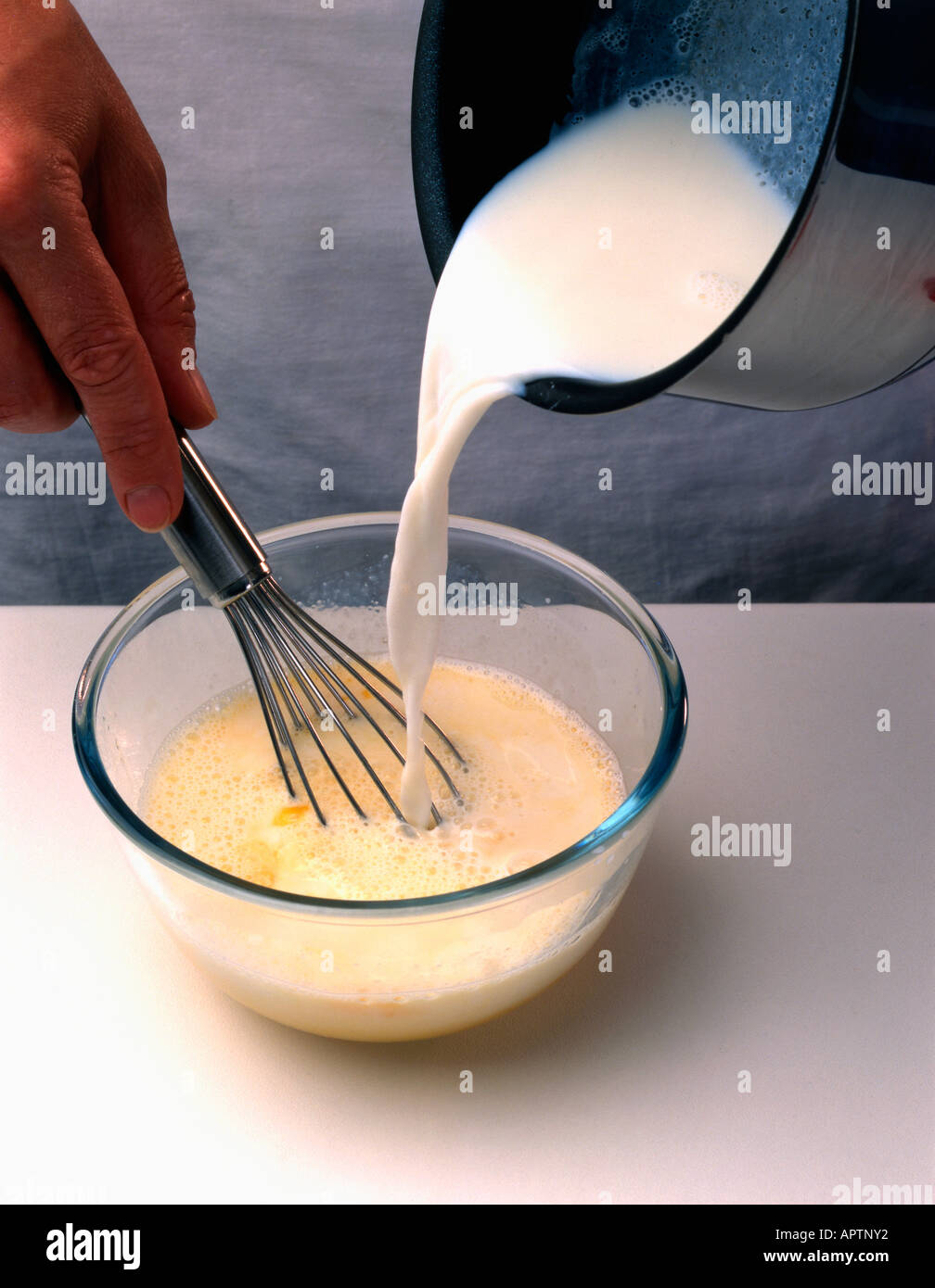 Making sweet egg sauce whisking hot milk into egg mixture Stock Photo