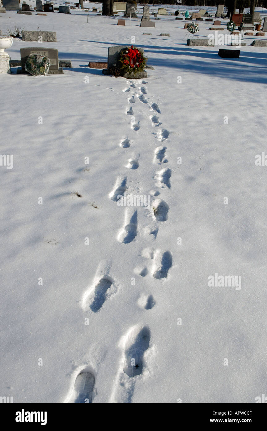 Footprints in the snow at winter time lead to a grave marker at a