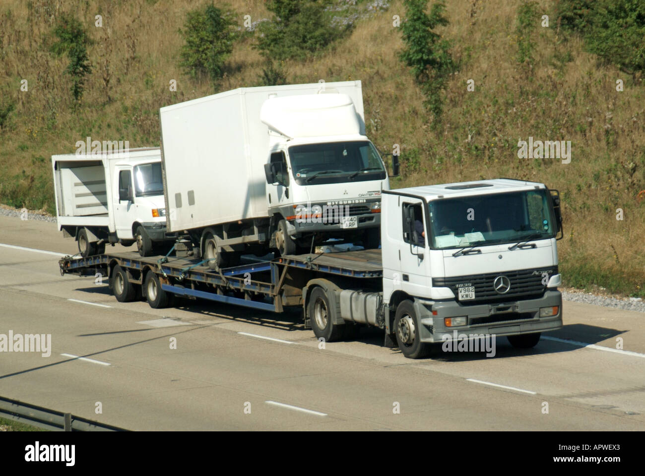M25 motorway unmarked white low loader transporting large van and milk float Stock Photo