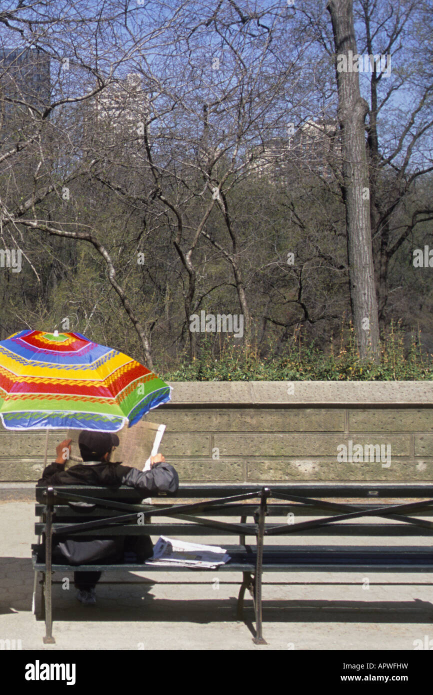 Man sitting under an umbrella reading a newspaper on a sunny day in ...
