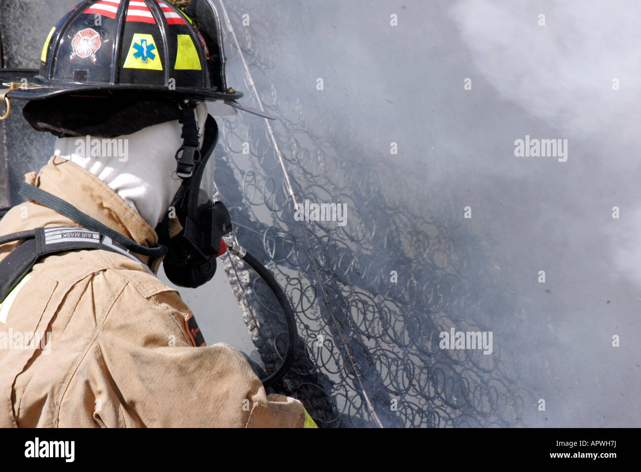 An American Firefighter removing a burnt mattress spring frame from the scene of an active fire