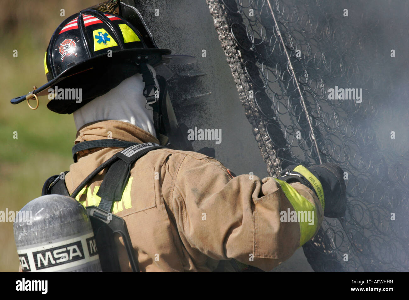 An American Firefighter removing a burnt mattress spring frame from the scene of an active fire