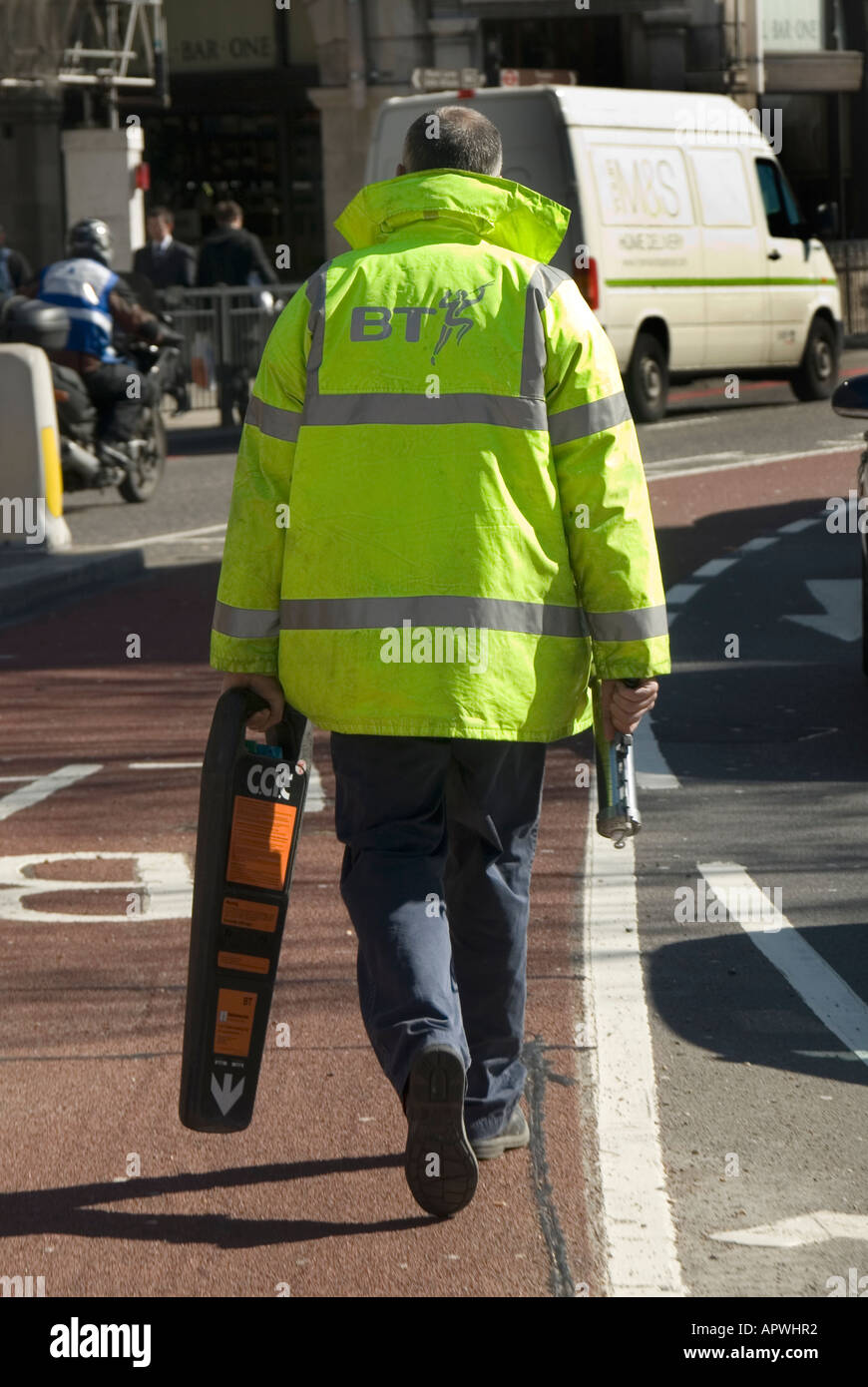 British Telecom technician BT high viz vis jacket at work walking in road holding scanning device helps to detect underground service cables London UK Stock Photo