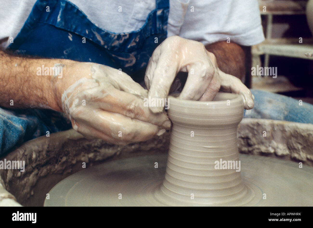 Clay covered hands of a potter making a clay pot on a potters electric