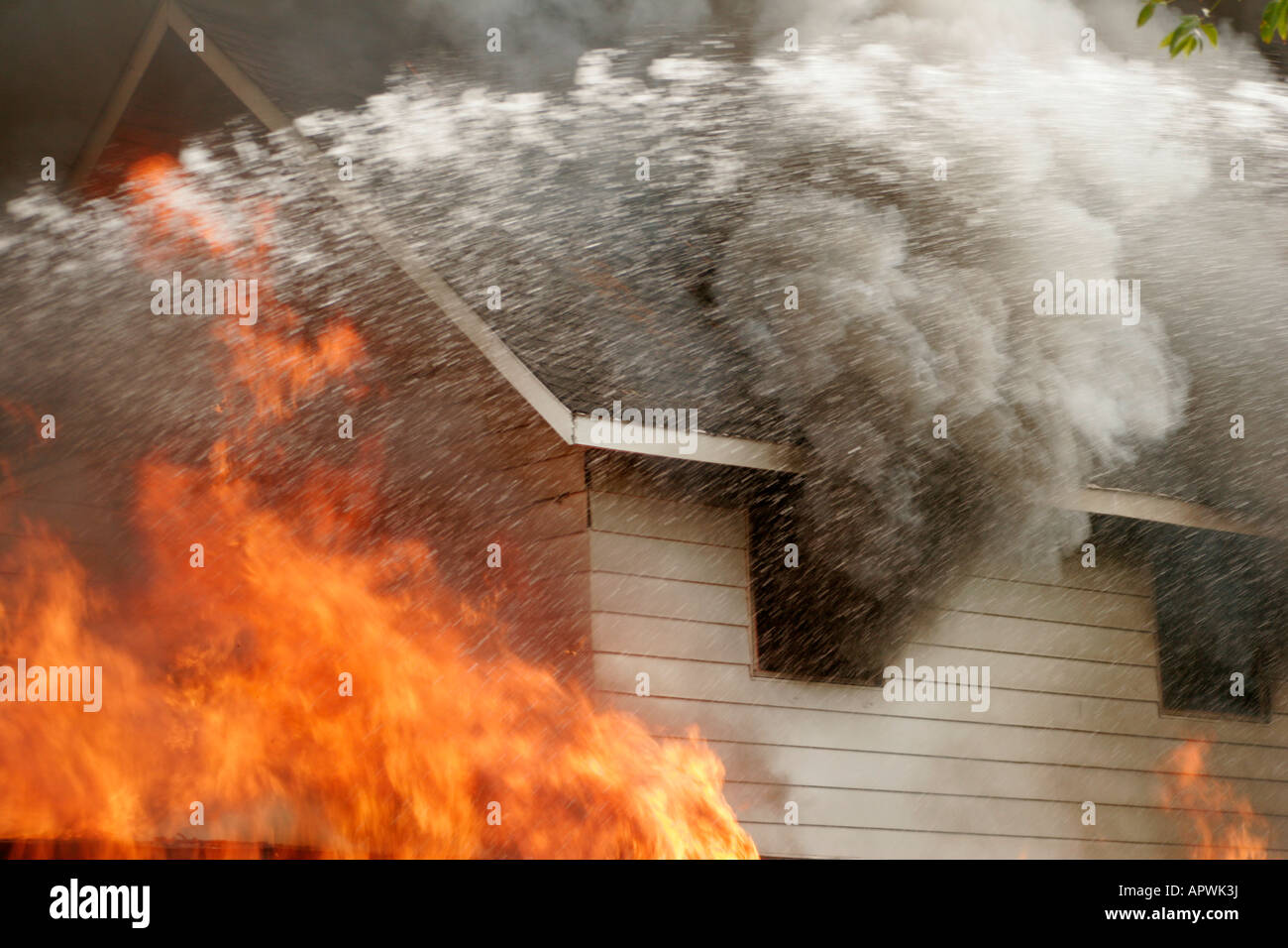 A house structure fire being attacked with water spray from the Fire Department ladder truck Stock Photo