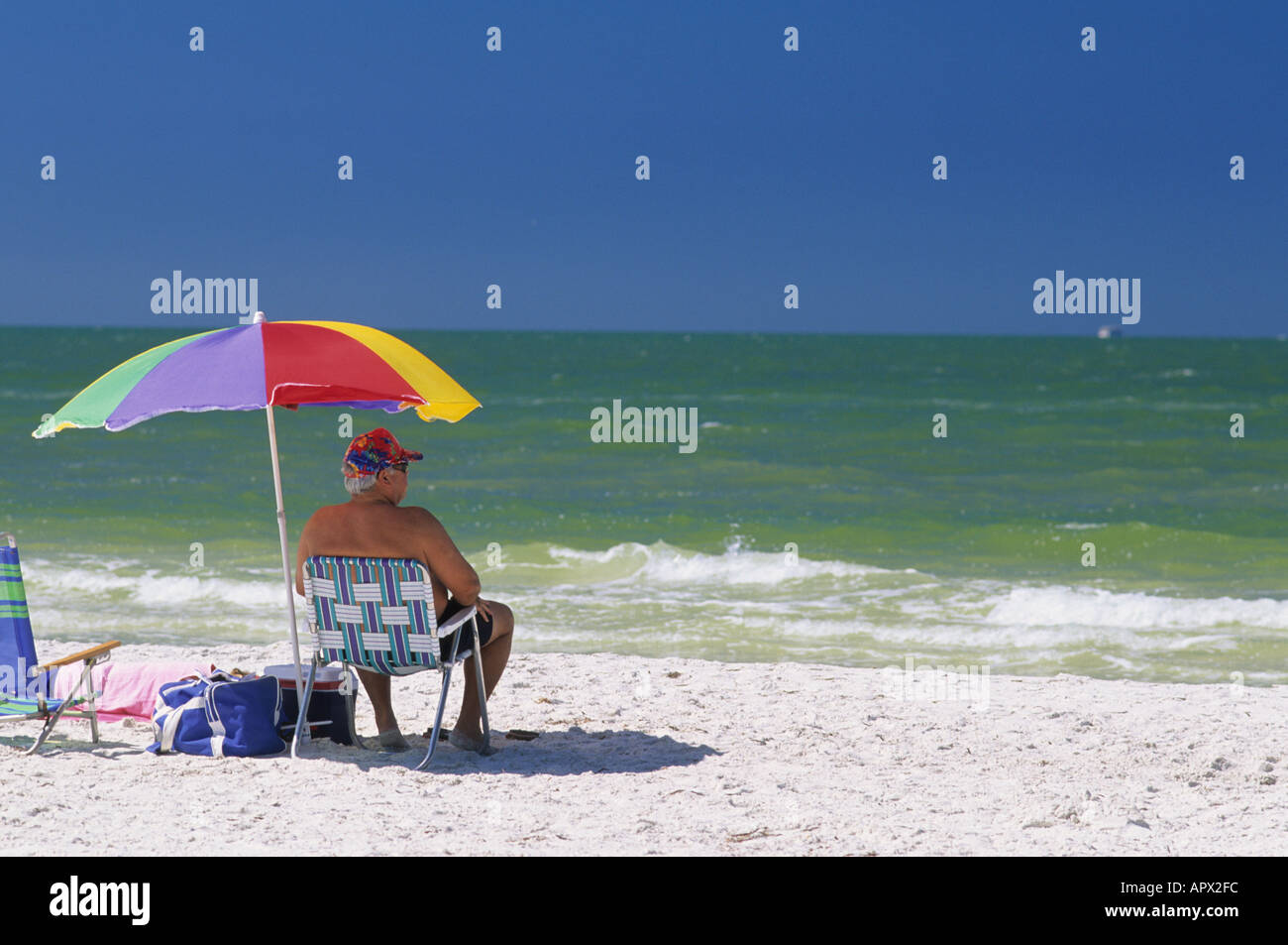 A senior citizen sitting under an umbrella at the beach in Clearwater
