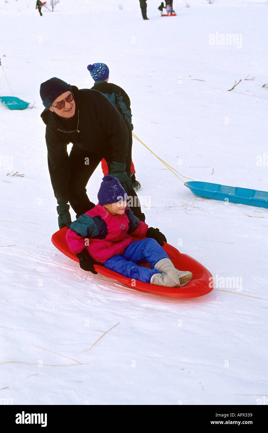 Grandfather pushing his granddaughter on sled in the snow Stock Photo