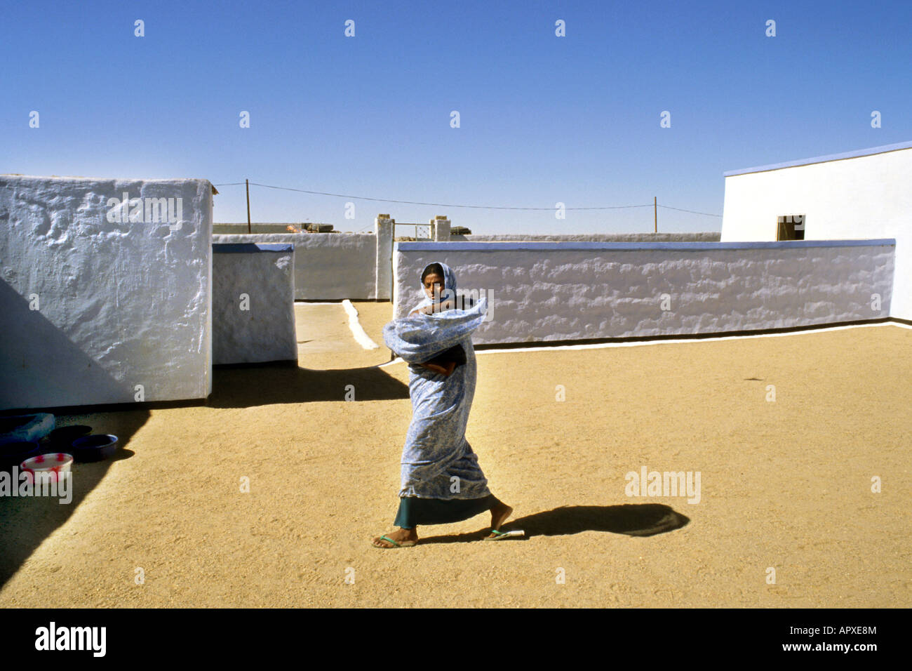 A young woman in traditional dress walks towards her house in a village courtyard in Tombos Stock Photo
