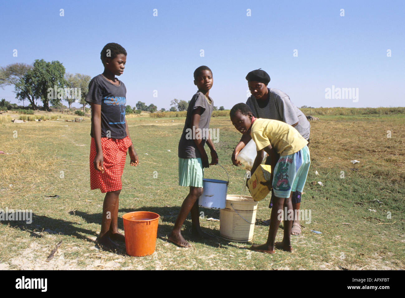 Girls helping their mother fill a bucket with water while collecting