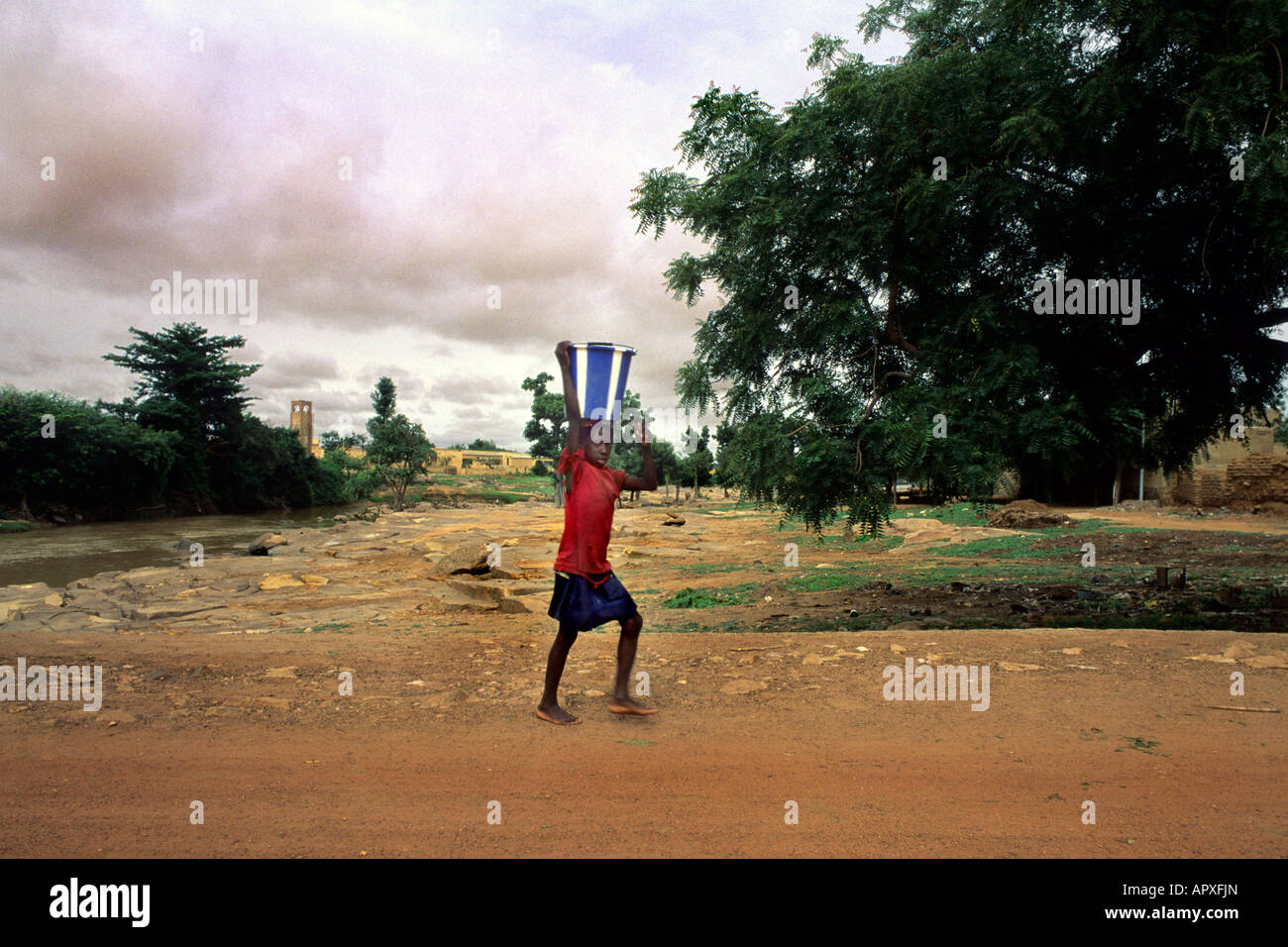 Young boy walking along a dust road balancing a bucket on his head