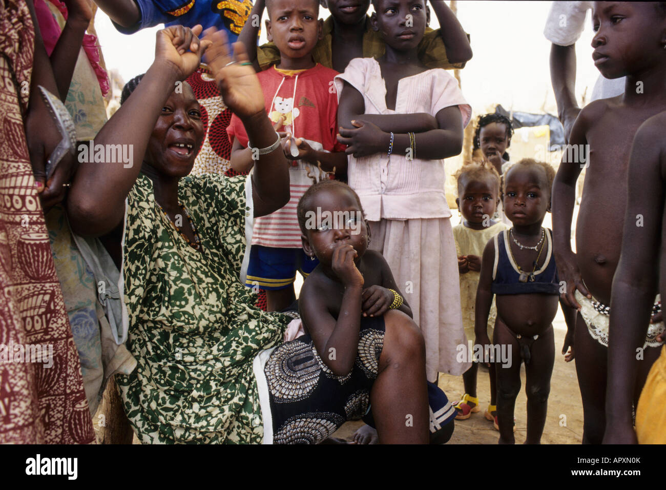Woman with arms raised in greeting and a large group of children standing around her Stock Photo