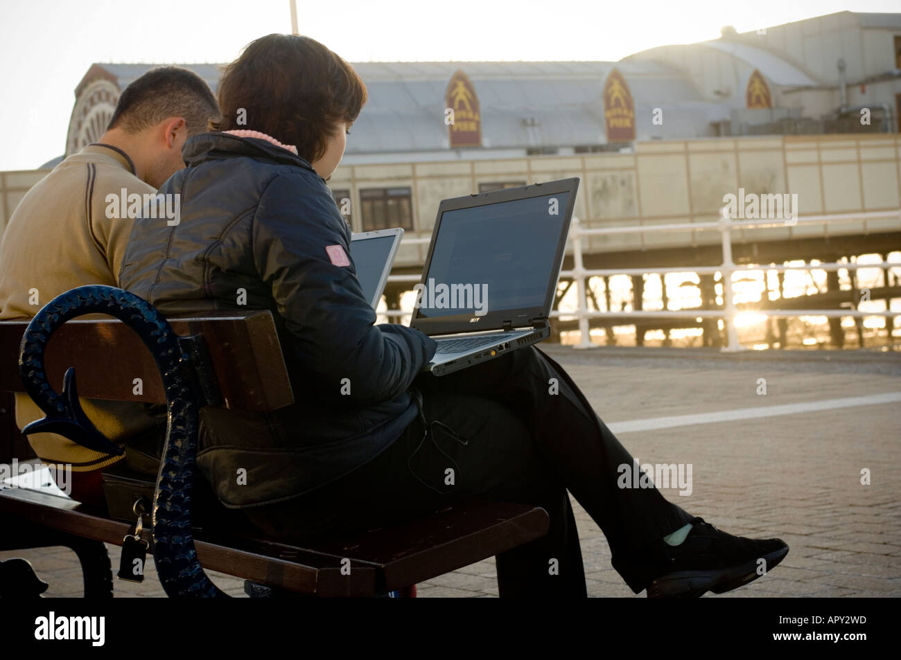 two polish young people using laptops to access wireless network Aberystwyth promenade to call home on Skype and send e-mail Stock Photo