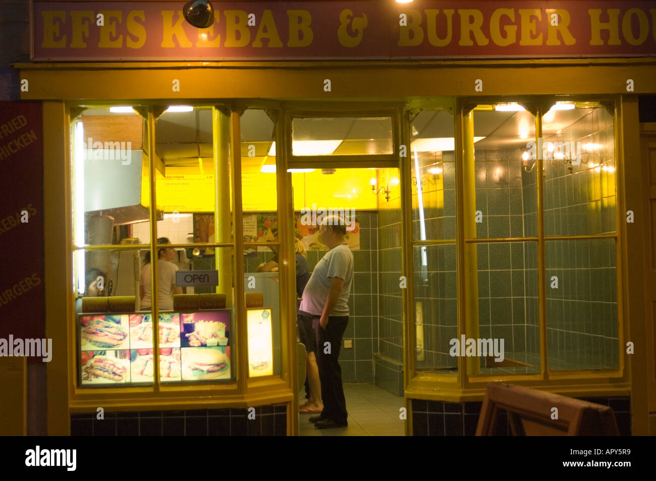 exterior image of fat man waiting to be served in kebab shop at night Aberystwyth Ceredigion wales UK Stock Photo