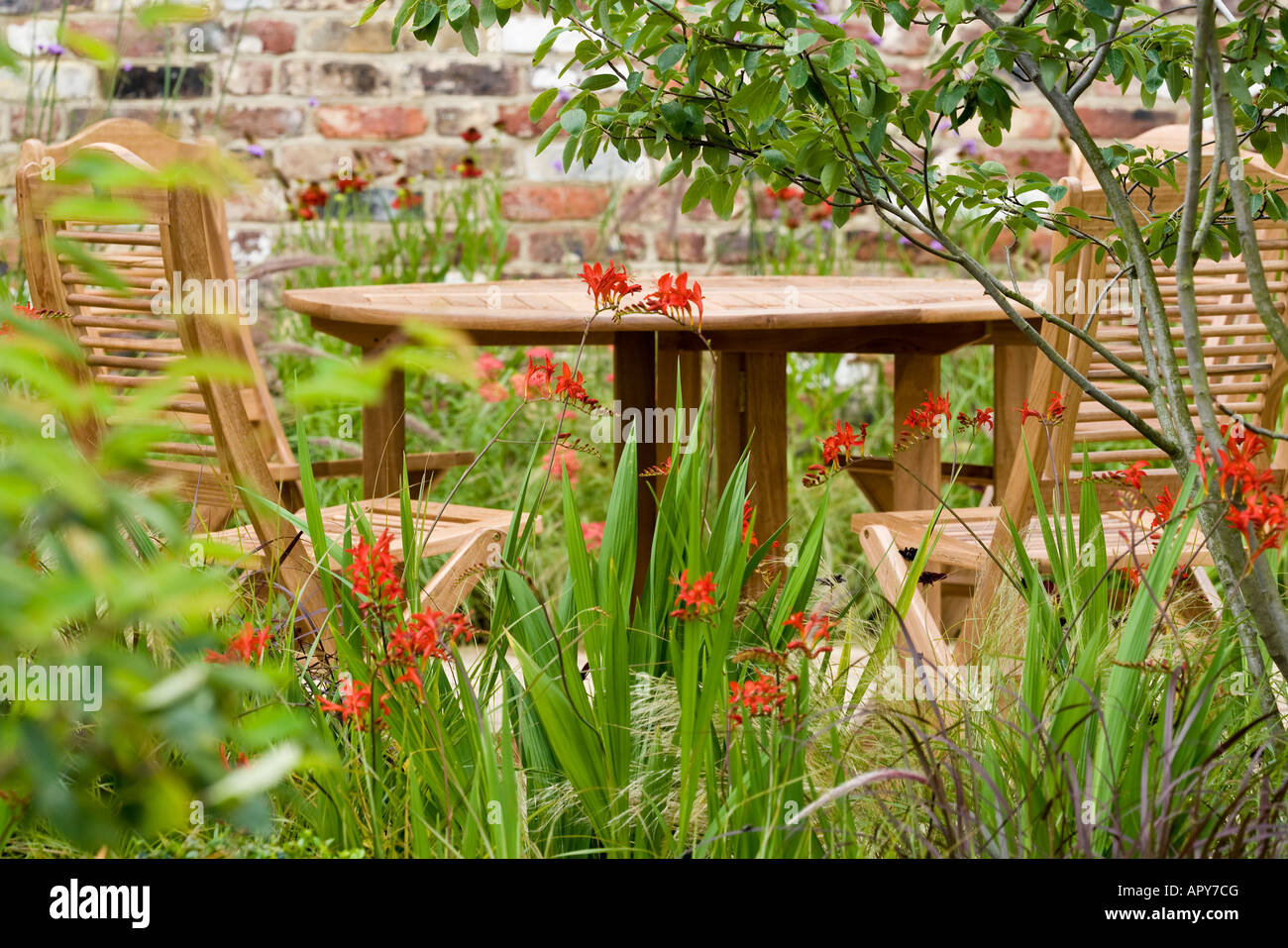 Table and chairs on sunny decking area in garden with flowers and