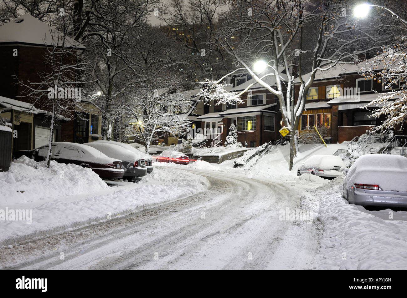 Covered with snow road and houses illuminated with street lights at ...