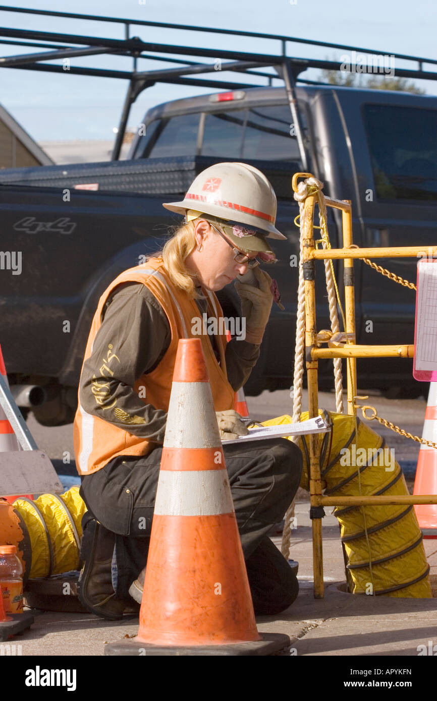 A female utility worker makes notes on her clipboard at the worksite