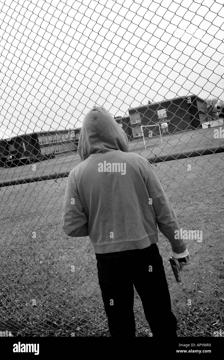 Lone male wearing hoodie and holding gun in front of high school Stock Photo