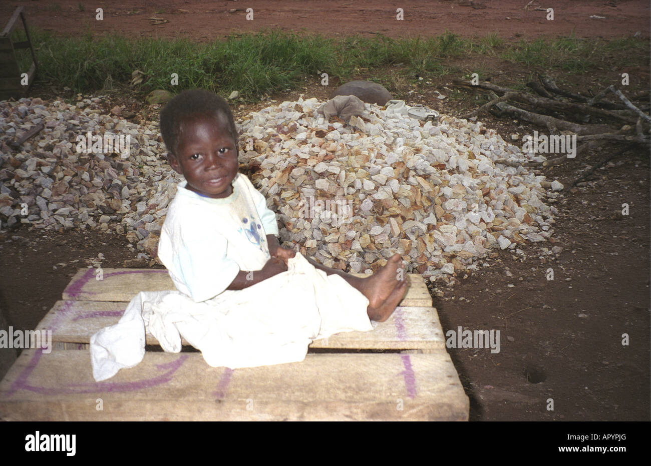 A baby sitting on a pile of stones where its mother is working as a stone breaker near Kumasi Ashanti Ghana West Africa Stock Photo