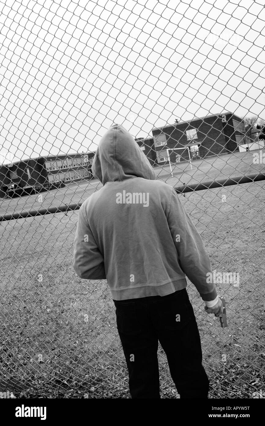 Lone male wearing hoodie and holding gun in front of high school Stock Photo