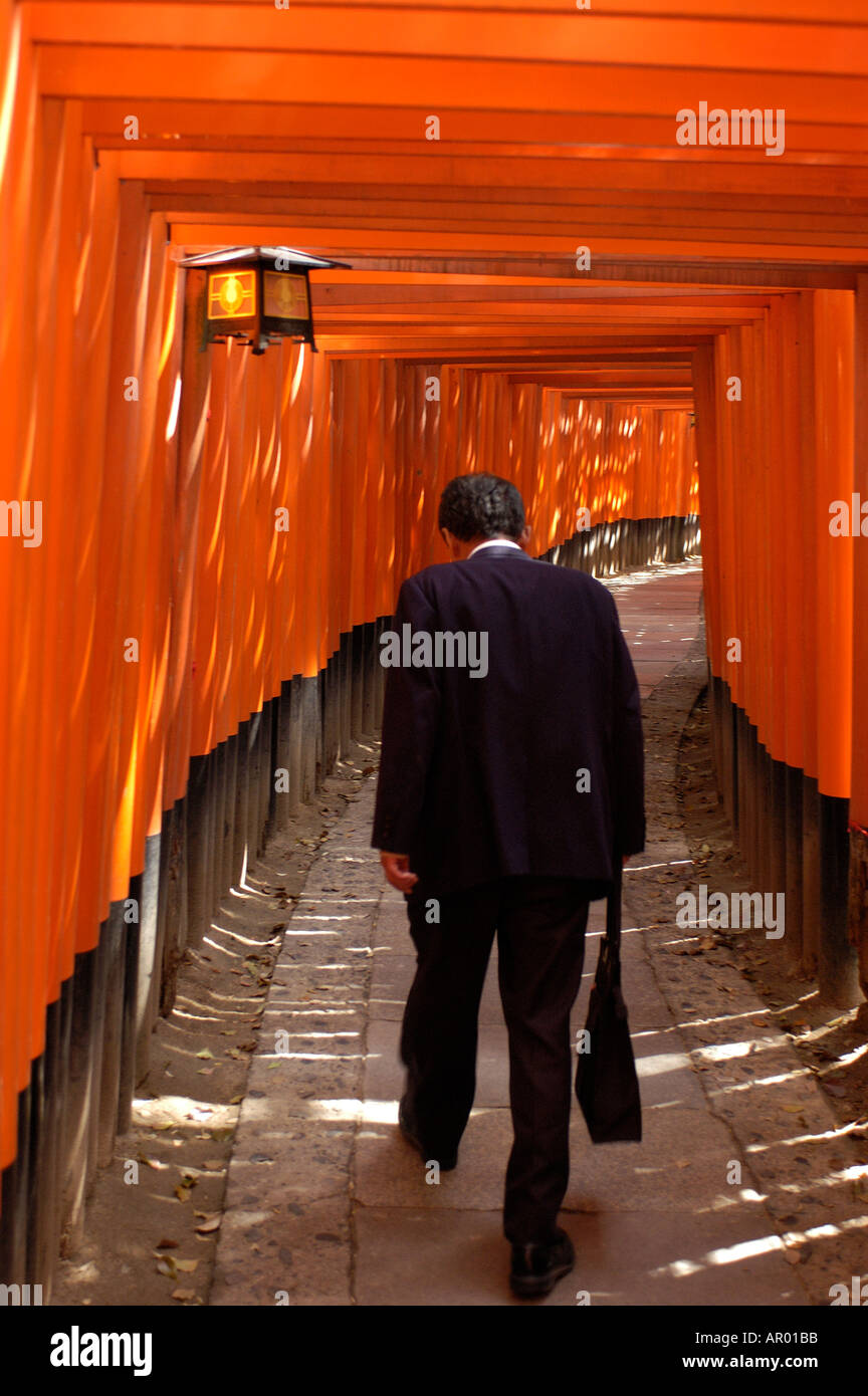 A businessman walks within hundreds of red Tori gates Fushimi Inari Shrine in Kyoto Japan Stock Photo