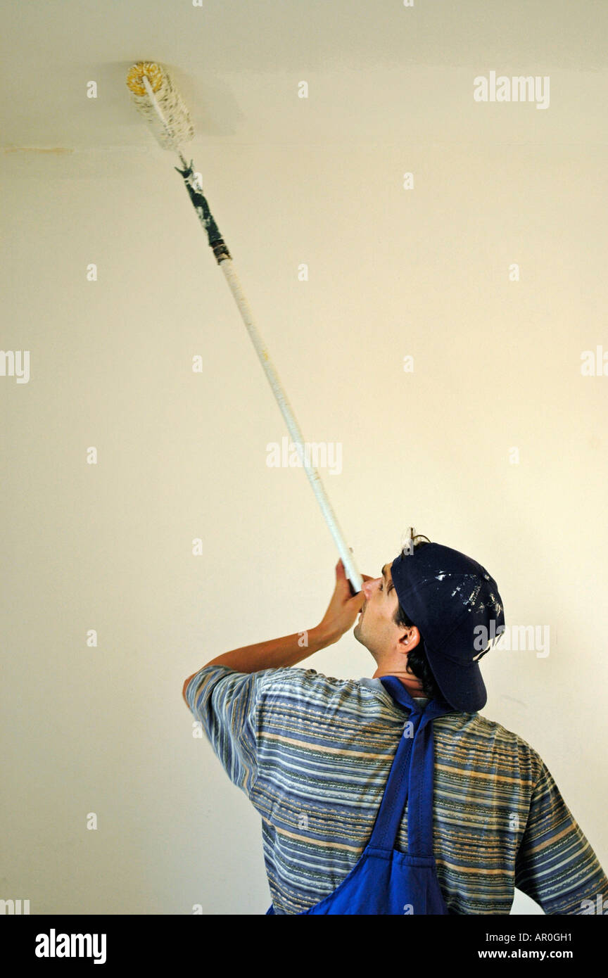 House painter in working clothes is painting the ceiling white Stock