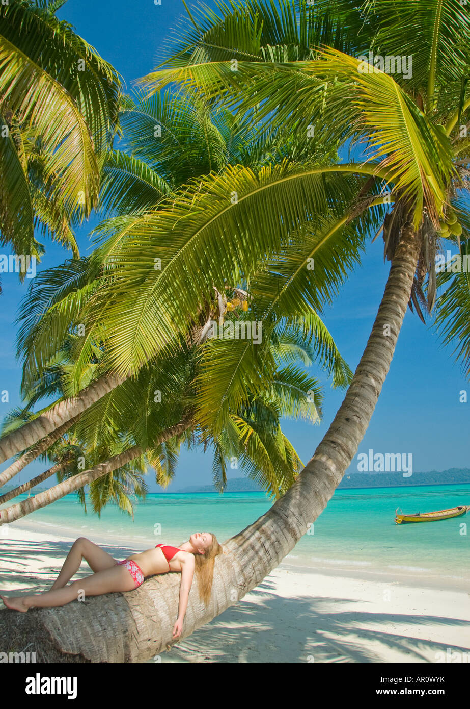 A woman in a red bikini relaxing under a palm tree on a beach in the Andaman Islands Stock Photo