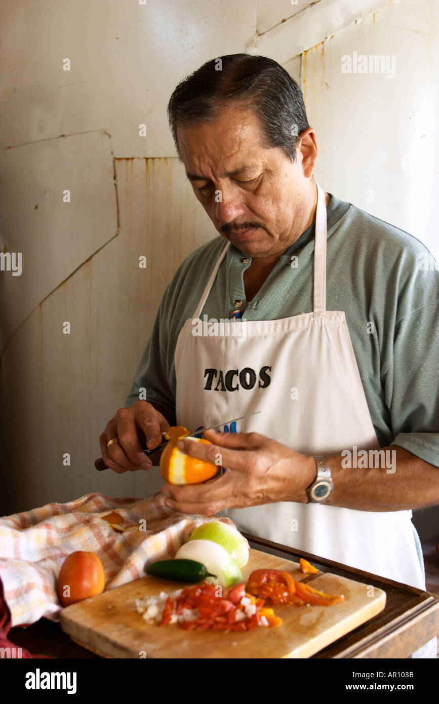 MEXICO Cabo San Lucas Man slice tomatoes in small restaurant kitchen