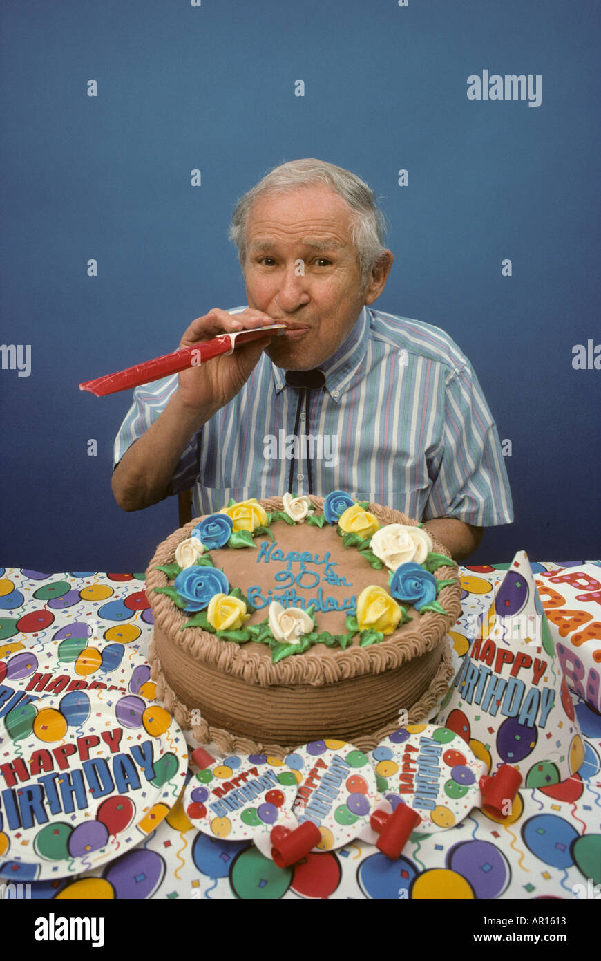 90 Year Old Man Blowing Noisemaker With Birthday Cake Stock Photo