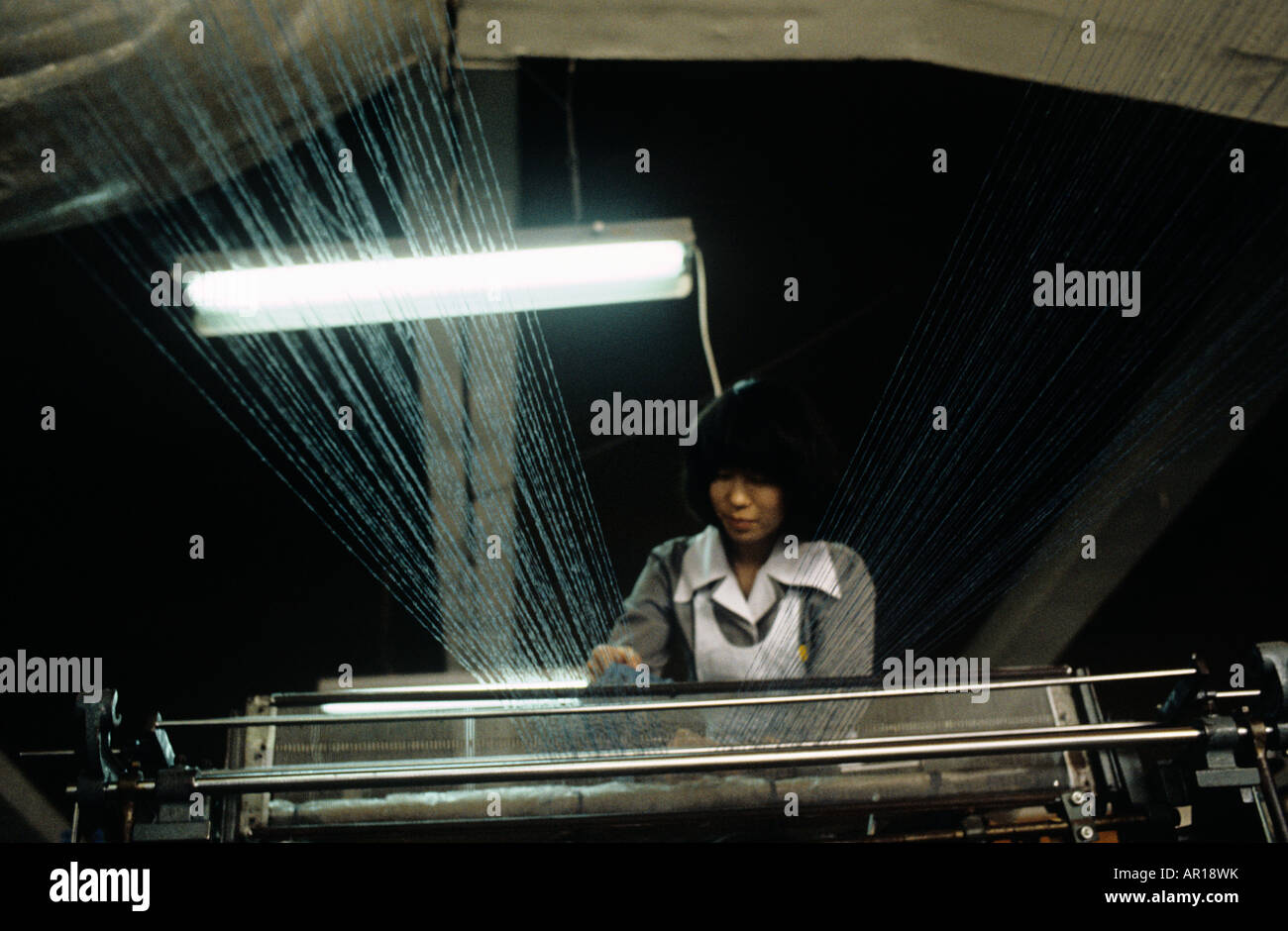 Korea. Girl at knitting machine in Knitting factory seen through lines