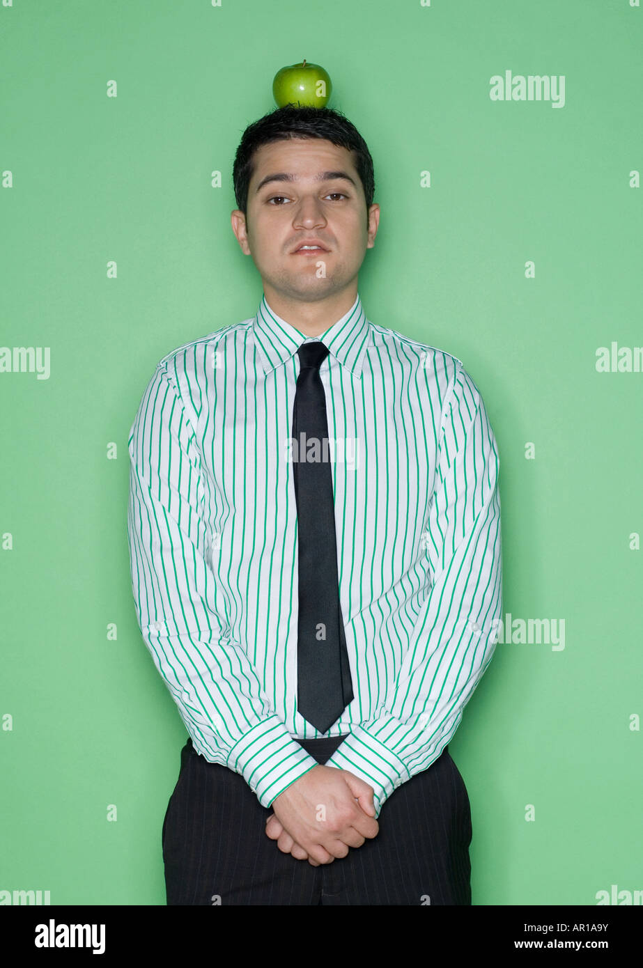 Portrait of a young man balancing a green apple on his head Stock Photo