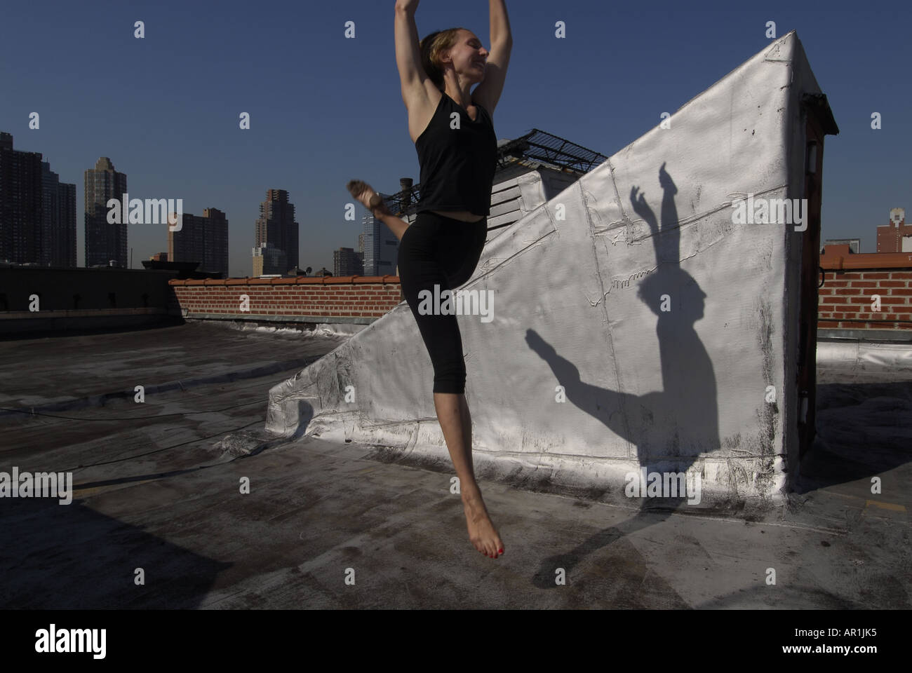Model released New York CIty Thirty years old blond woman dancing on a building roof in a sunny morning in mid town Manhattan exercise healthy athletic strech strenching strong fit American health cardiac vascular lifestyle move movement power yogi twist mujer americana rubia ejercicio sana nueva y ork movimiento estiramiento salud medicina estilo de vida feliz saludable fuerte Stock Photo