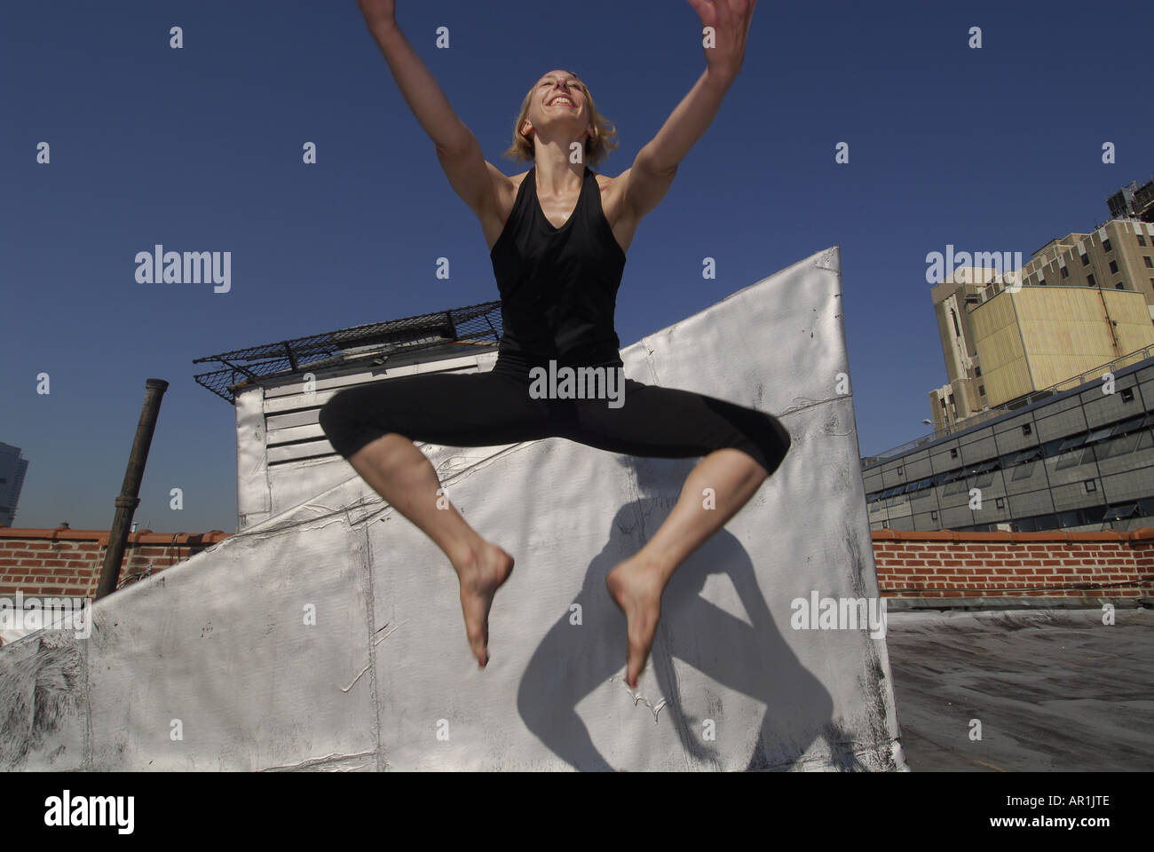 Model released New York CIty Thirty years old blond woman dancing on a building roof in a sunny morning in mid town Manhattan exercise healthy athletic strech strenching strong fit American health cardiac vascular lifestyle move movement power yogi twist mujer americana rubia ejercicio sana nueva y ork movimiento estiramiento salud medicina estilo de vida feliz saludable fuerte Stock Photo