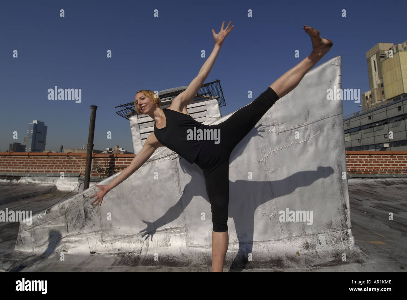 Model released New York CIty Thirty years old blond woman dancing on a building roof in a sunny morning in mid town Manhattan exercise healthy athletic strech strenching strong fit American health cardiac vascular lifestyle move movement power yogi twist mujer americana rubia ejercicio sana nueva y ork movimiento estiramiento salud medicina estilo de vida feliz saludable fuerte Stock Photo