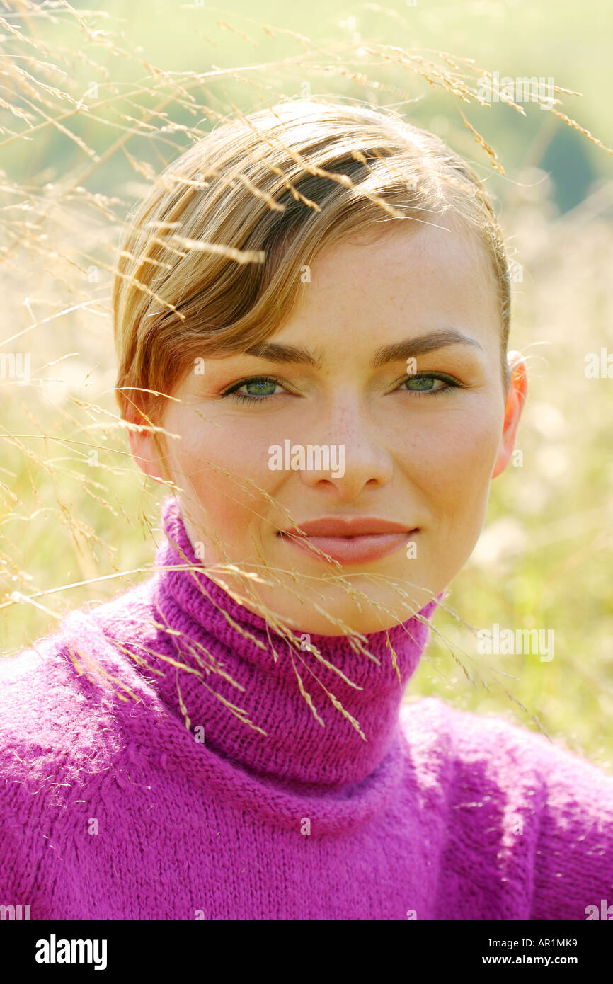 outdoor autumn day mead field grass close up woman young 25 30 blonde forelock portrait sweater jersey golf pink smile smilin Stock Photo