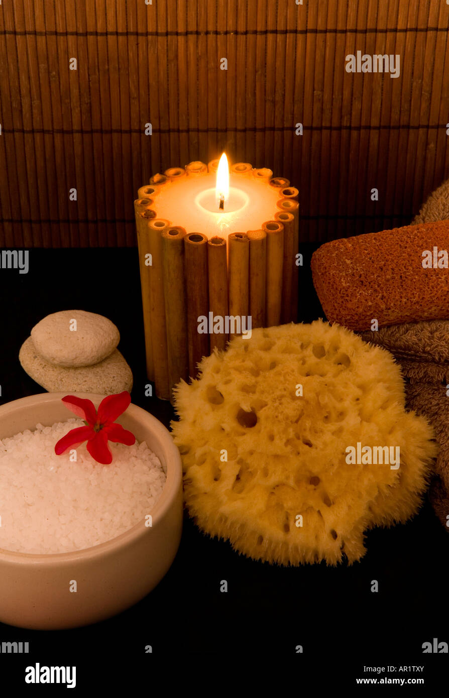 Spa setting with aromatic candles, sea salts, a natural sponge, body scrubs and folded towels. Stock Photo