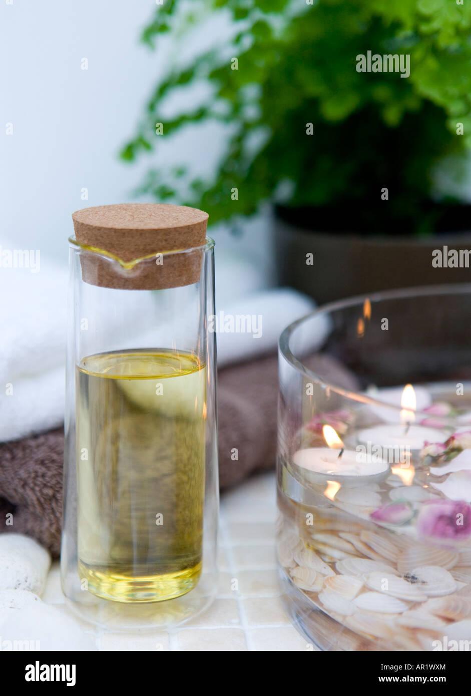 Spa setting with floating candles and fresh rose petals in a glass bowl,  folded towels, and massage oil (sweet almond oil) Stock Photo