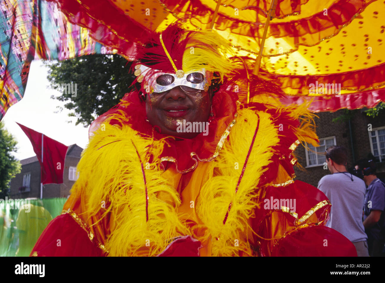 An Afro-Carribean woman in bright feathered costume and head gear wearing a silver mask at the annual Notting Hill Carnival Stock Photo