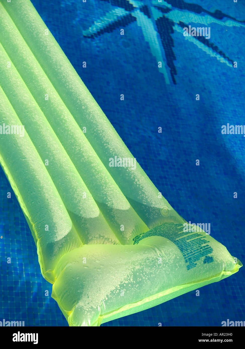 Yellow green inflatable lilo in blue tiled swimming pool Stock Photo