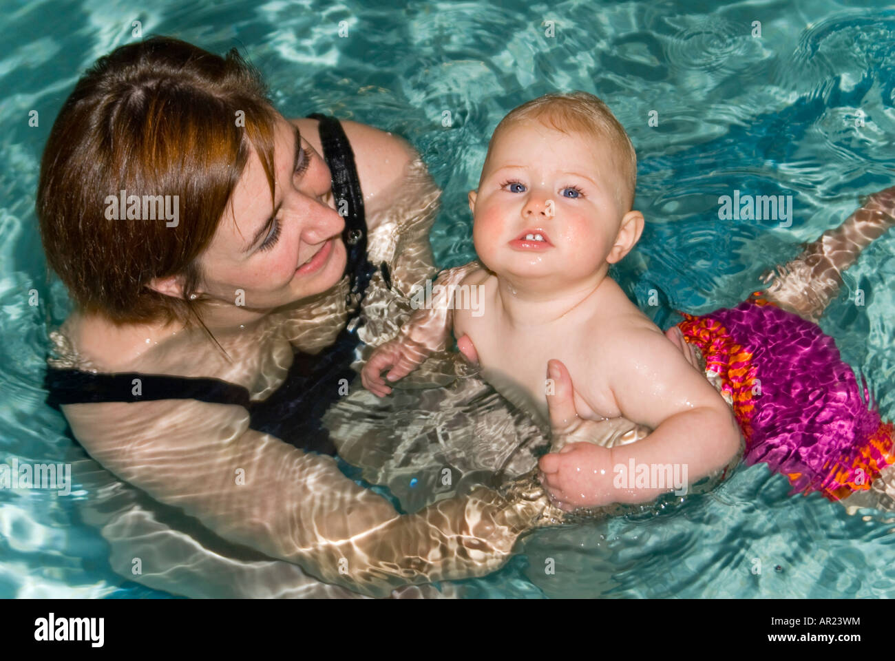 Horizontal close up of a young Caucasian mother and her baby daughter in a swimming pool participating in a  swimming class Stock Photo
