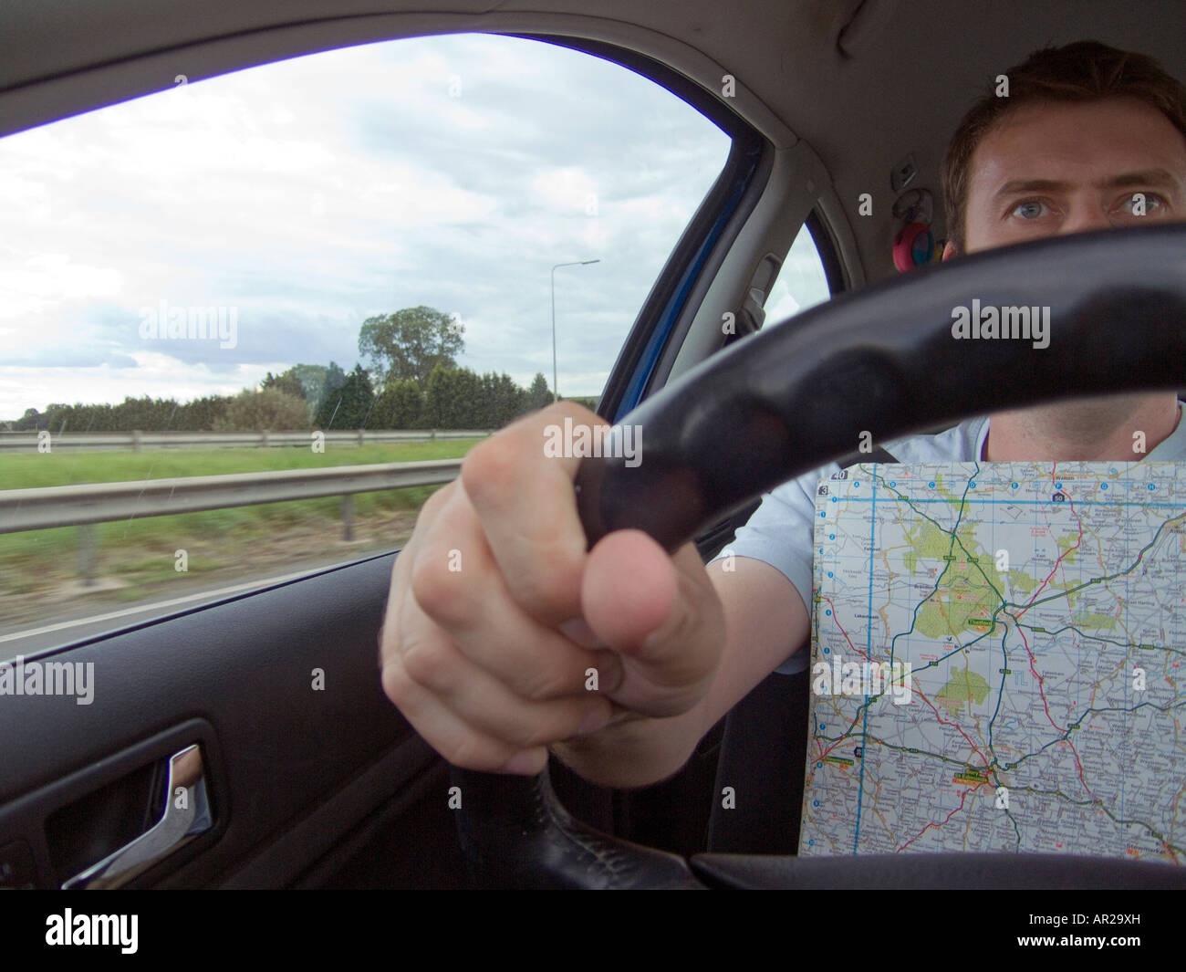 A driver drives a car whilst reading a map for directions, close up view from interior Stock Photo