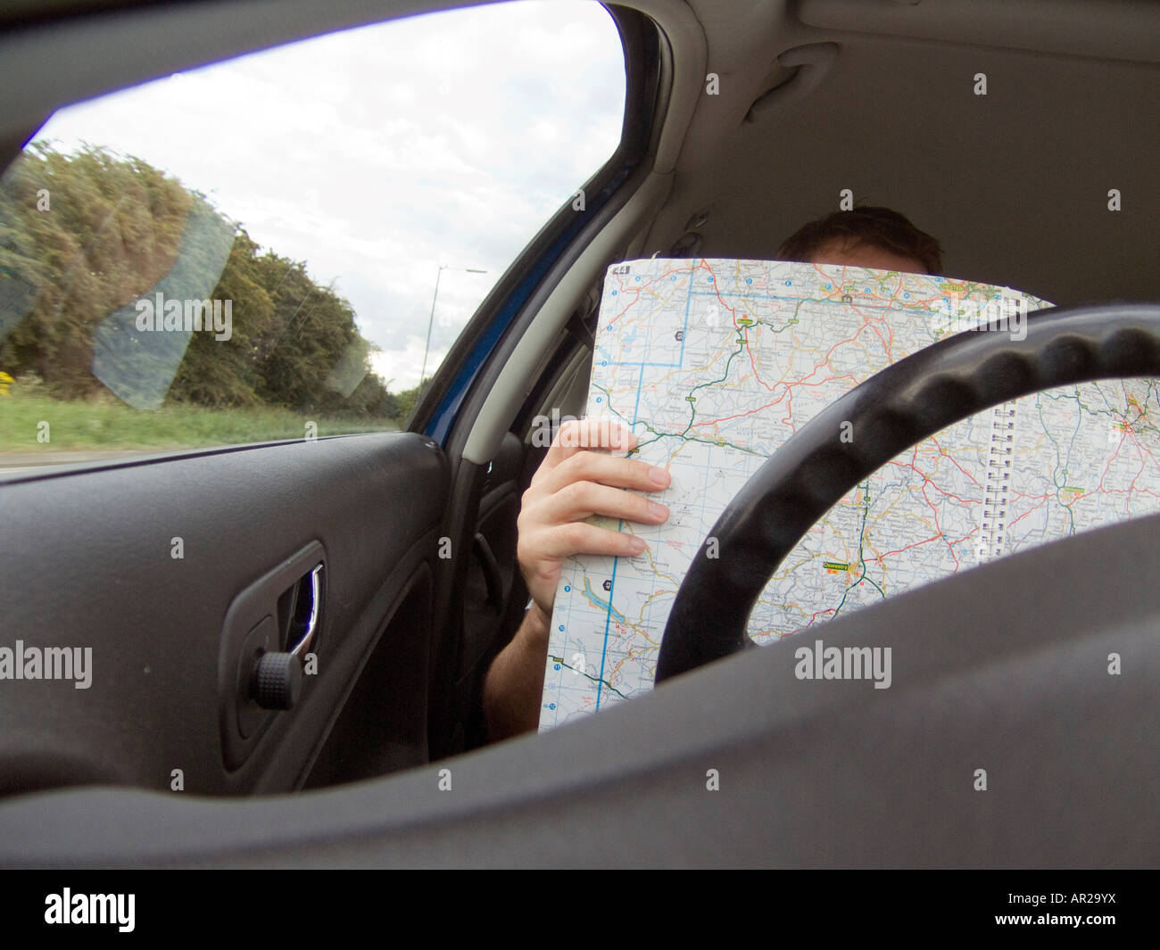 A driver drives a car whilst reading a map for directions, close up view from interior Stock Photo