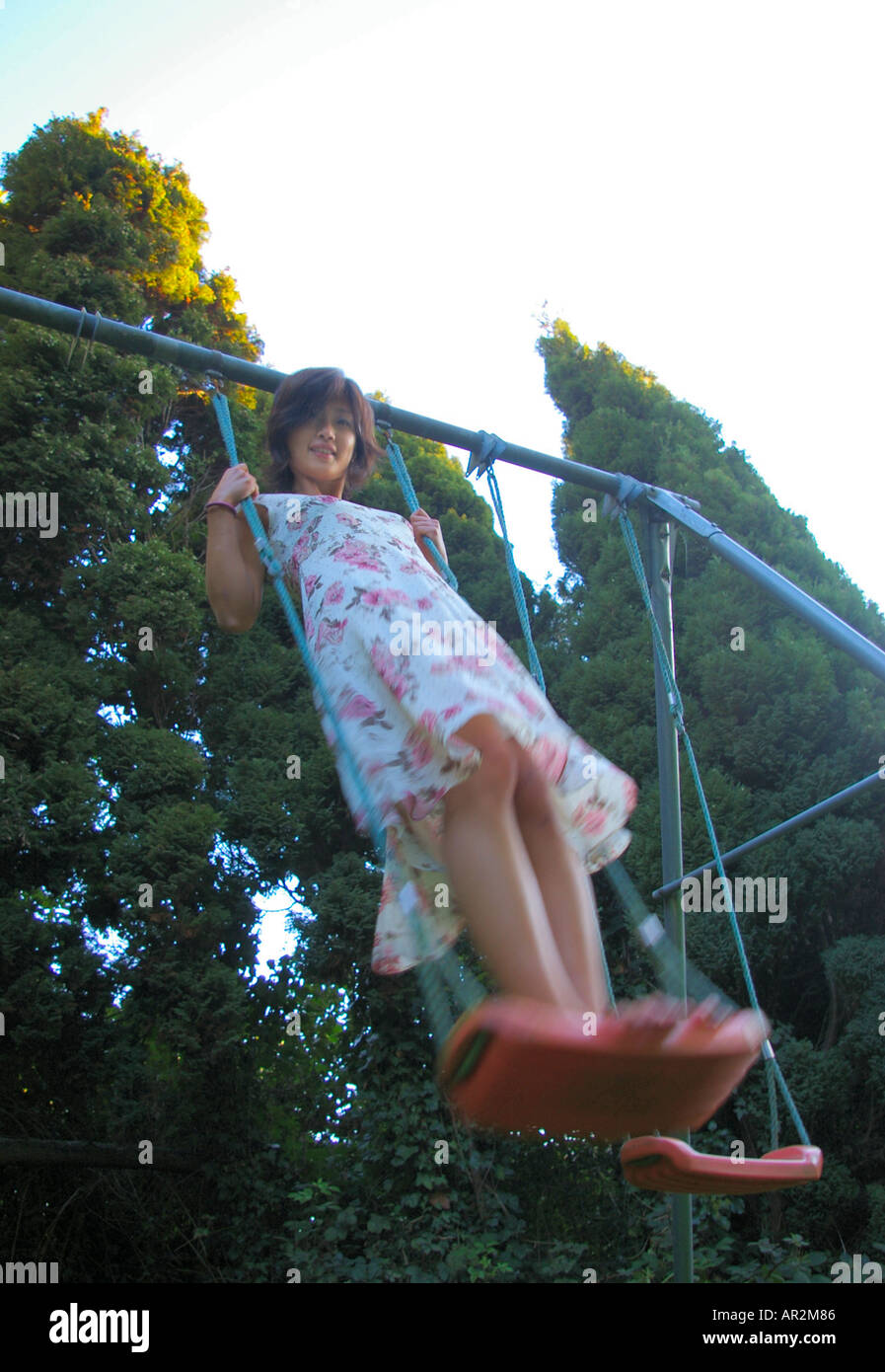 Krean Asian woman in flowery dress on garden swing, some motion blur Stock Photo