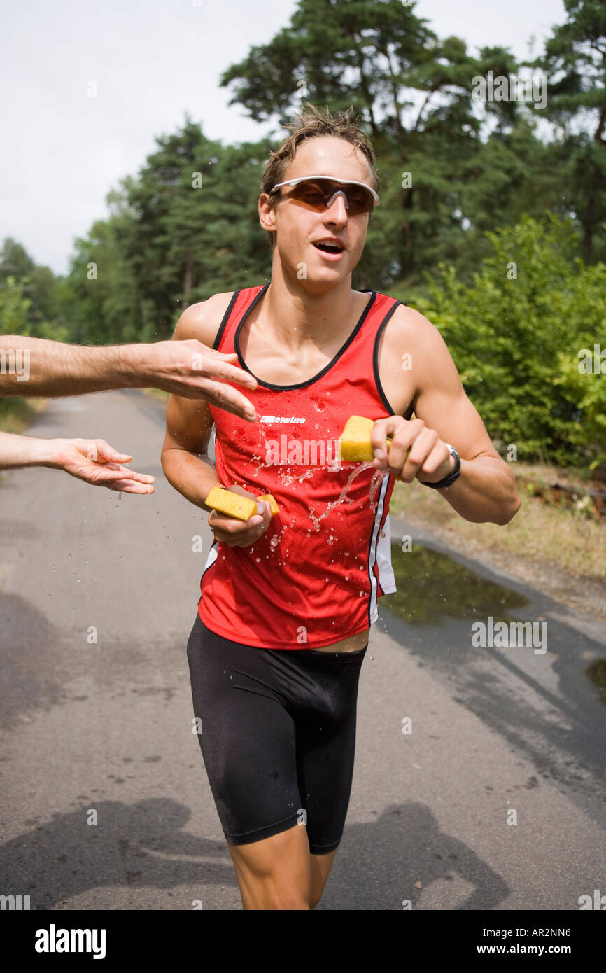 Young man running and holding wet sponges during sports race Stock Photo