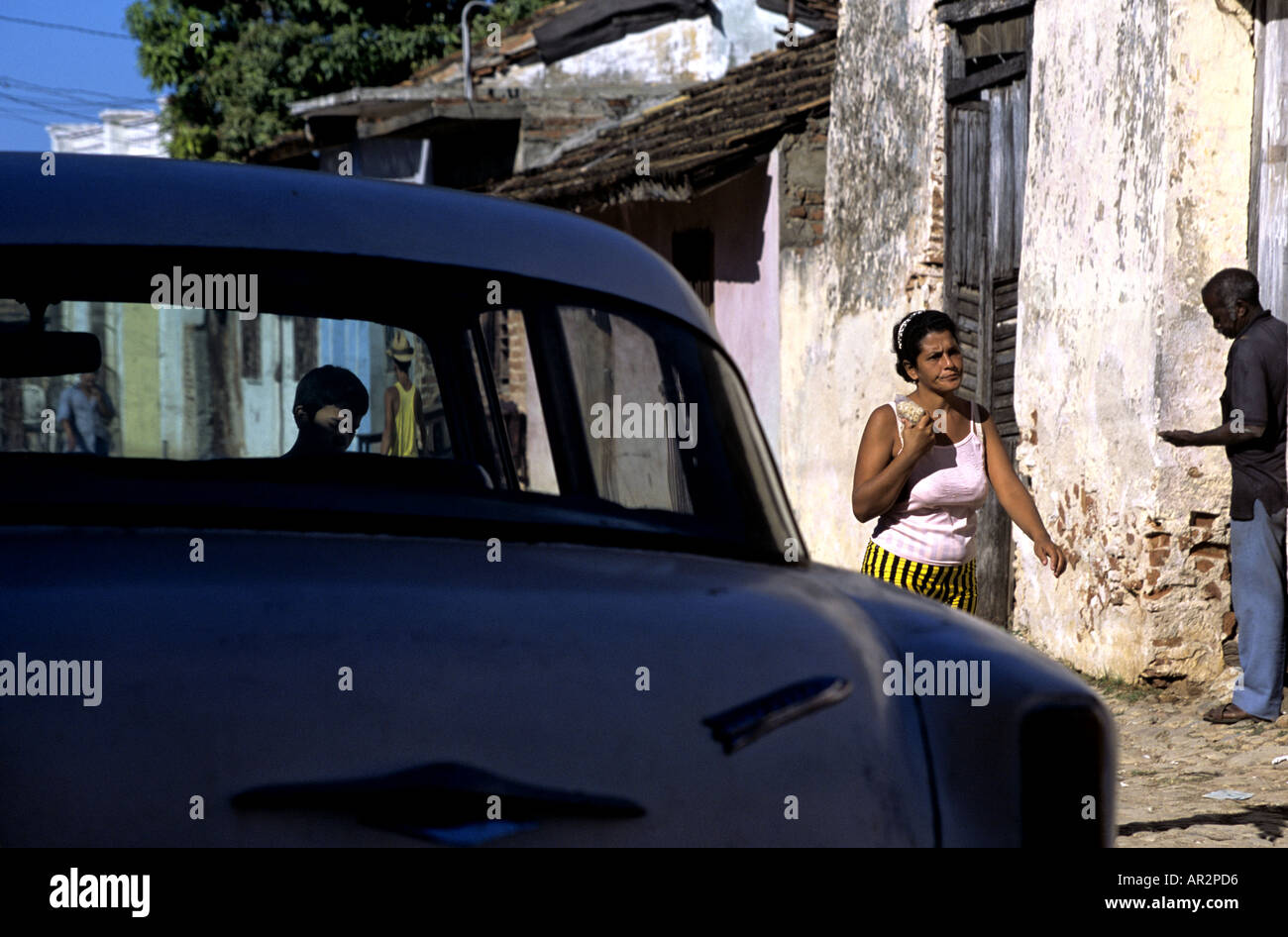 Woman in gold & black striped spandex walking past blue classic 50s car in Trinidad, Cuba. Stock Photo