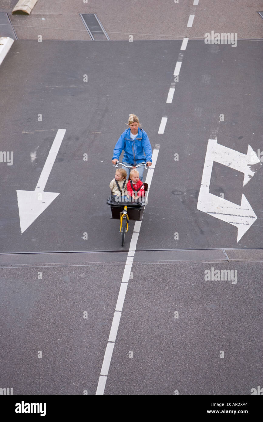 HOLLAND AMSTERDAM MOTHER WITH TWO CHILDREN ON A CARGO BIKE CYCLING OVER A DOUBLE TWO WHITE ARROWS AND A SINGLE ARROW SIGN PAINTED ON THE ROAD Stock Photo