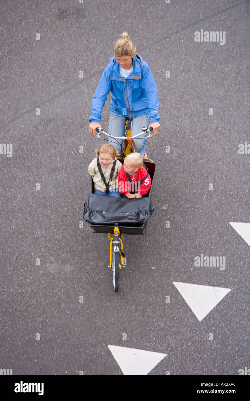 HOLLAND AMSTERDAM MOTHER WITH TWO CHILDREN ON A CARGO BIKE CYCLING OVER WHITE TRIANGLES SIGN PAINTED ON THE ROAD Stock Photo