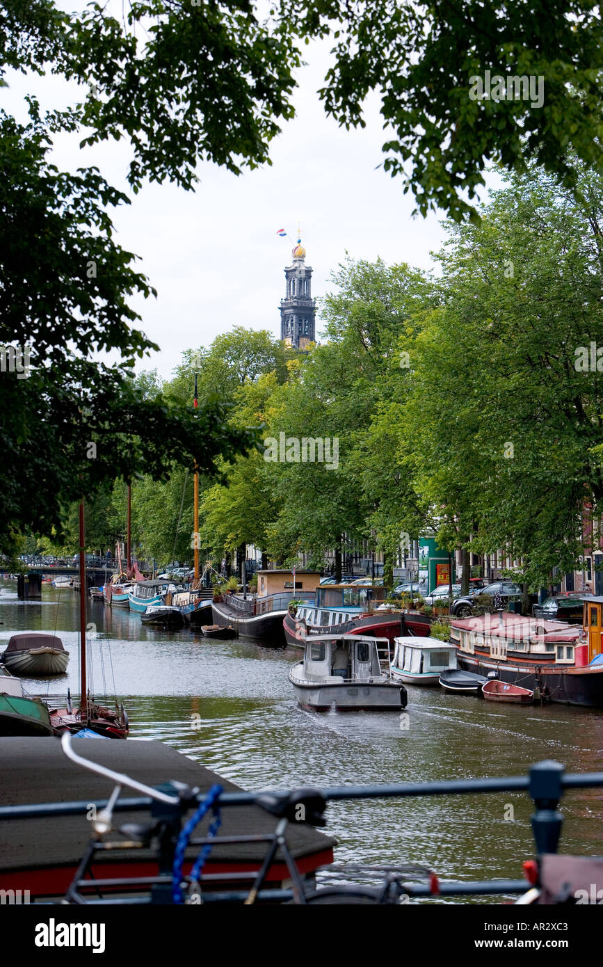 HOLLAND AMSTERDAM CANAL WITH TREES AND WESTERTOREN WEST TOWER CHURCH SPIRE WITH DUTCH NATIONAL FLAG Stock Photo